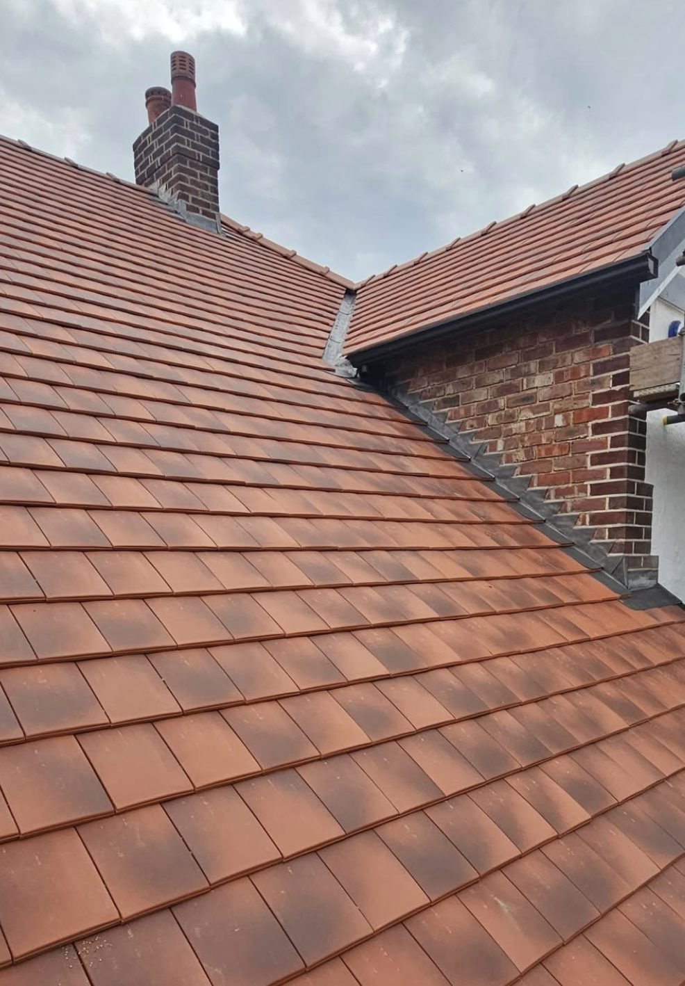 Clay tiles with stepped lead flashing running up brickwork