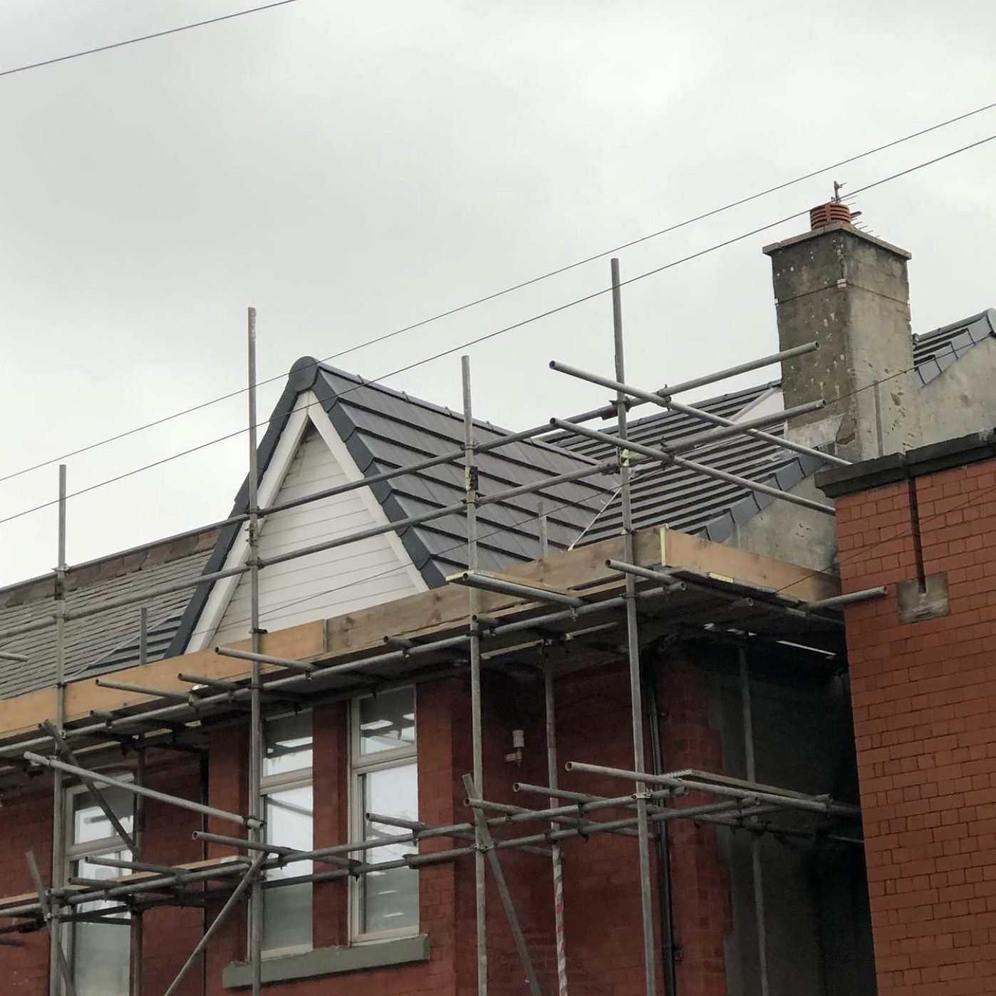 Tiled gable-fronted dormer on a red-brick building behind scaffold