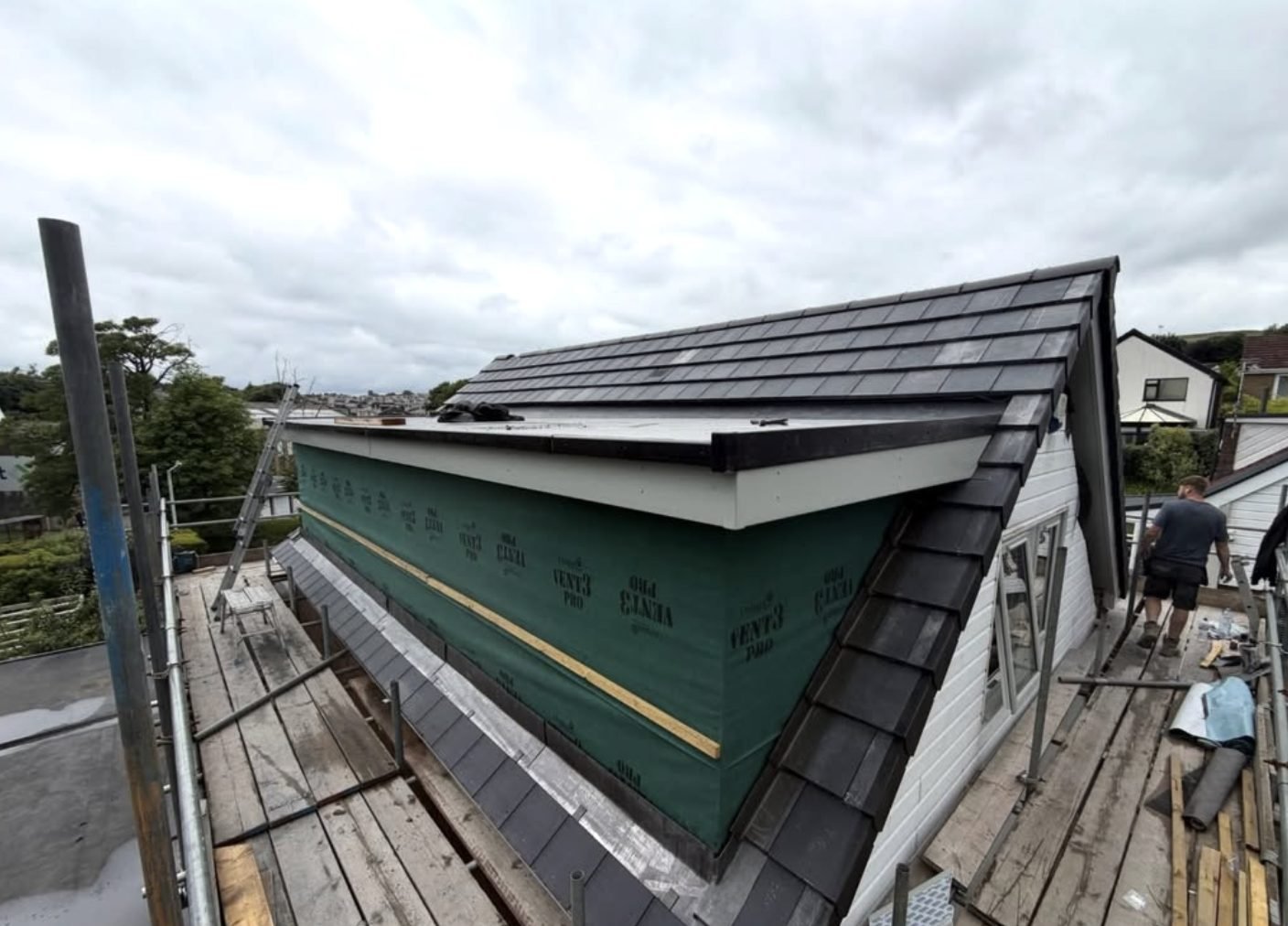 Roofer on scaffold beside a dormer being tiled, membrane on the dormer face