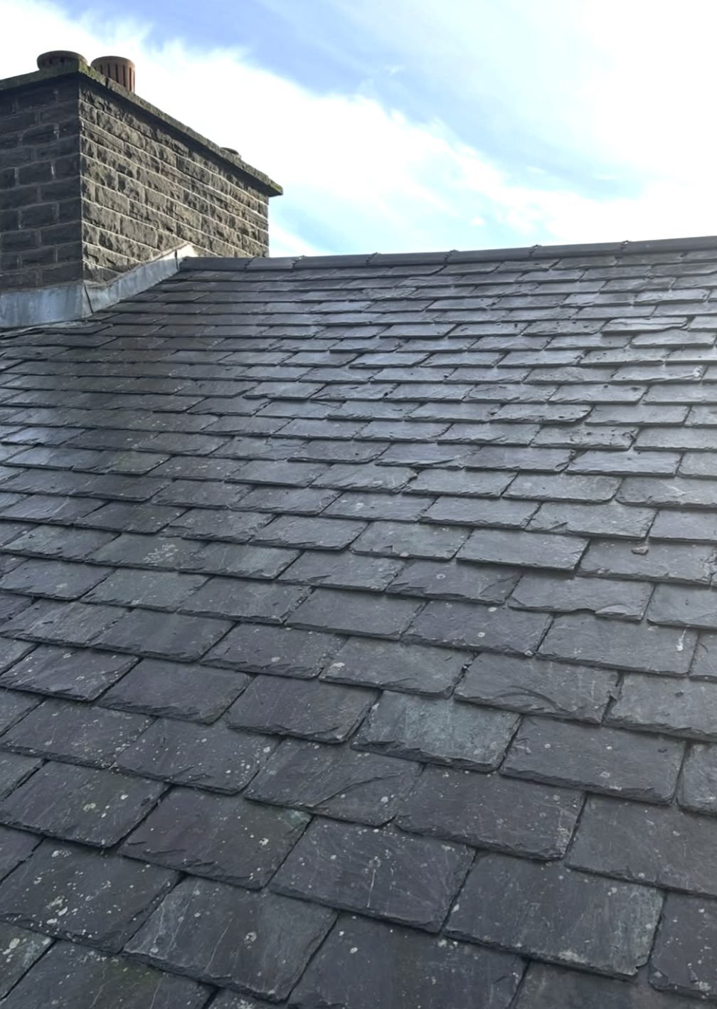 Weathered natural slate roof with lead flashing at a stone chimney