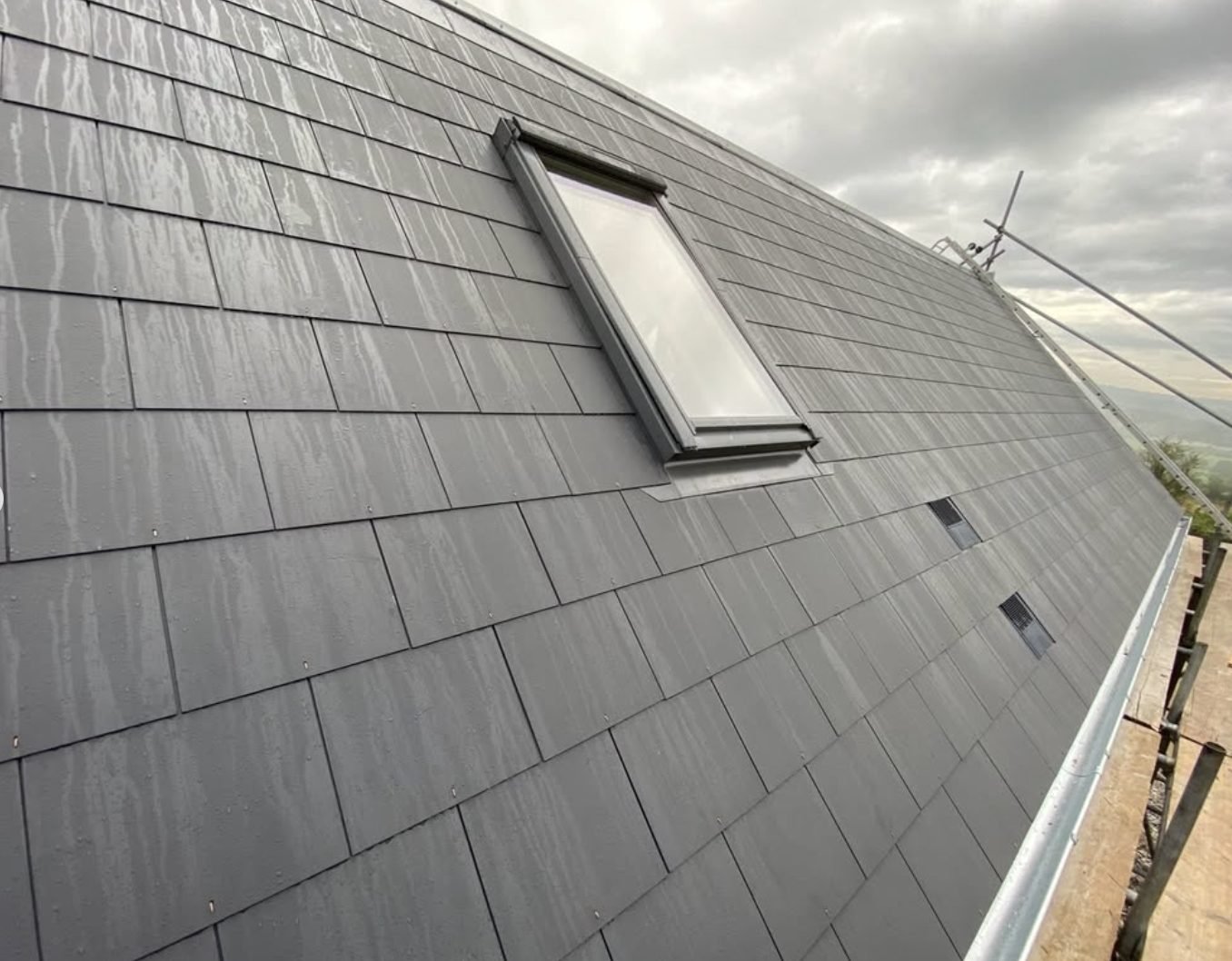 Slate roof finished around a roof window with slate vents above the gutter