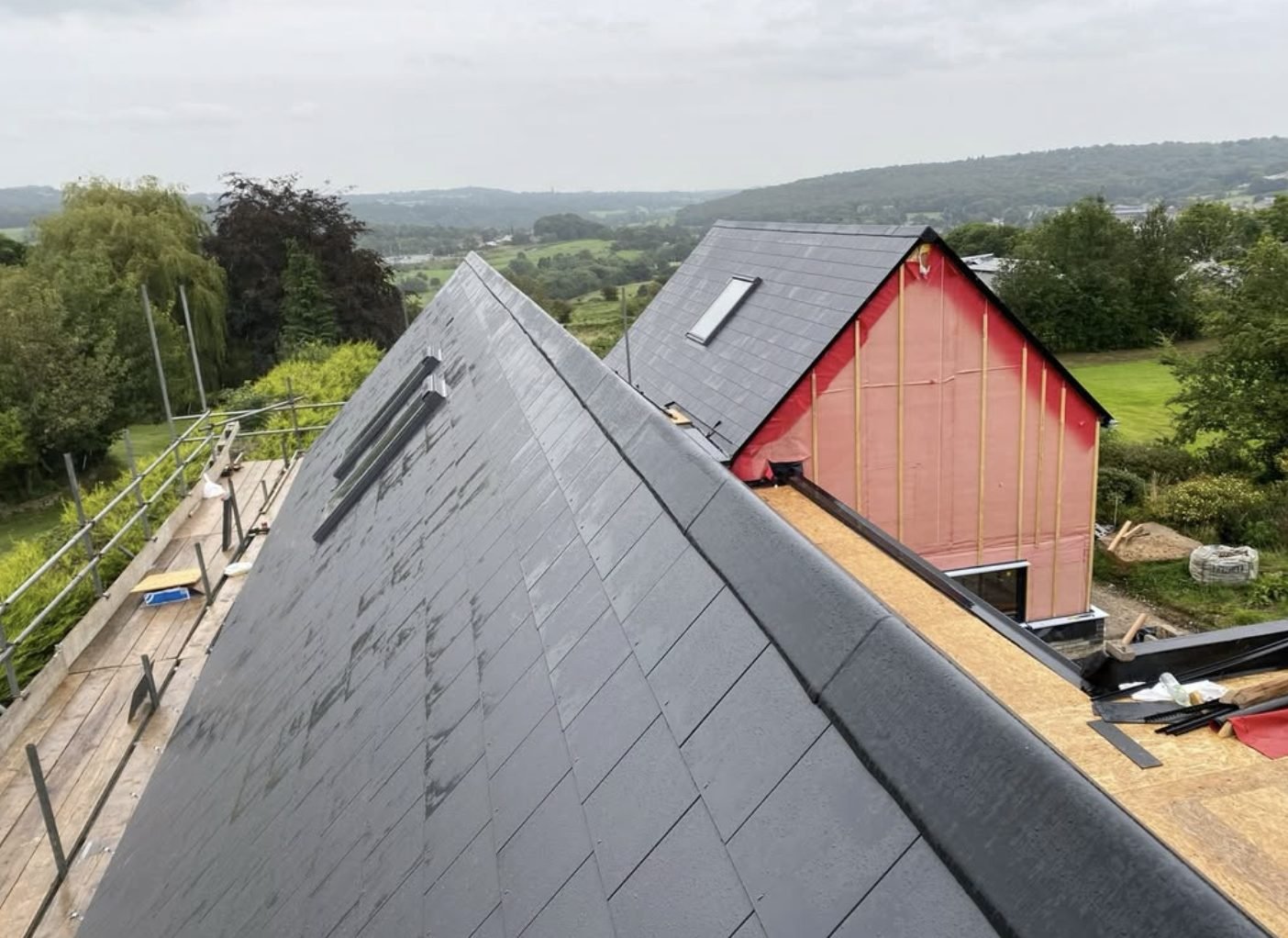 Slated roof with two rooflights and scaffold, looking out over a green valley