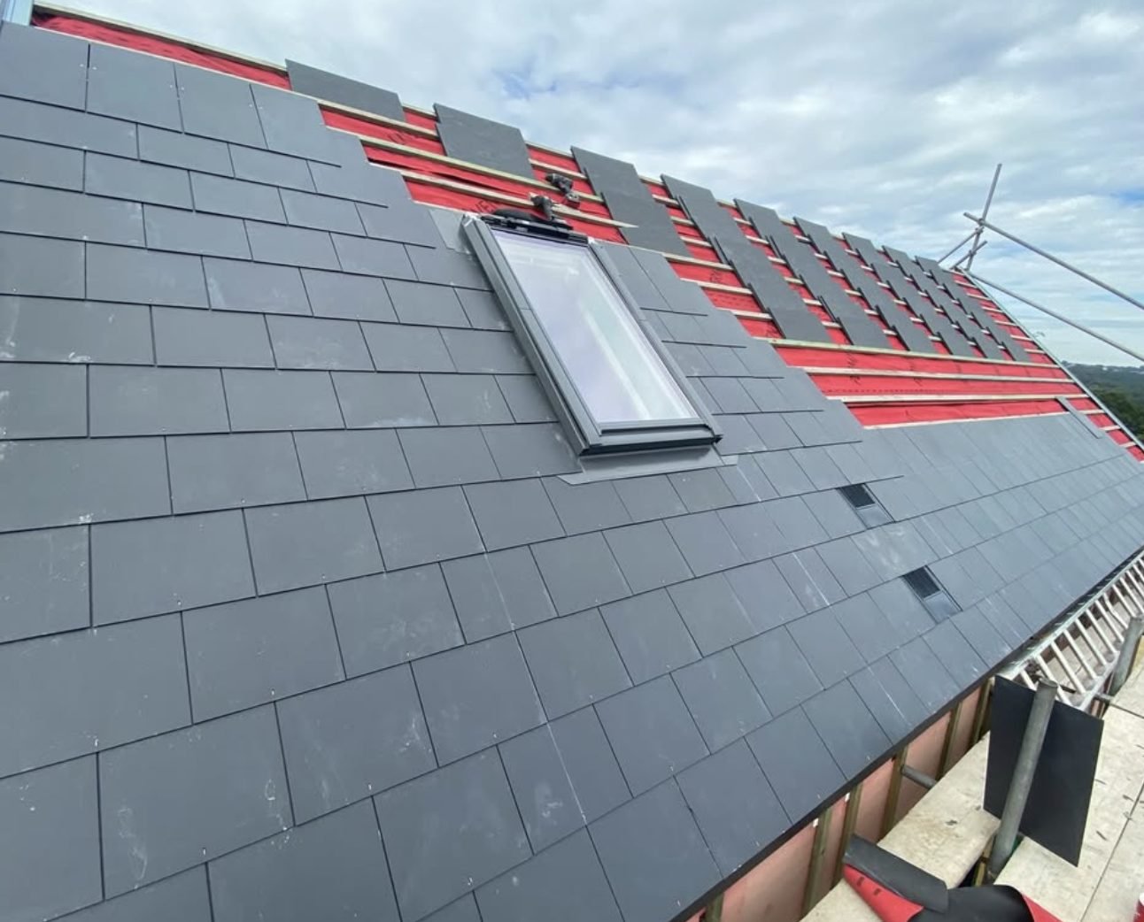 Roof being slated over red membrane and battens around a new roof window
